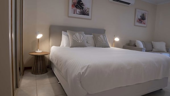 Ein Hotelzimmer mit einem großen Bett, zwei Nachttischen mit Lampen, einem Sofa und Kunstwerken an den Wänden.