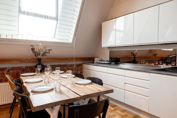 Una cocina moderna con armarios blancos, una mesa de comedor de madera dispuesta para cuatro comensales y un tragaluz.