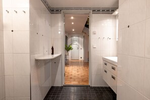 Un pasillo estrecho con paredes de baldosas blancas, suelo de madera y una puerta blanca al final.