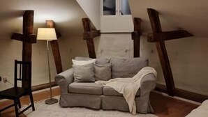 Et hyggeligt rum med en grå sofa, et lille bord, en gulvlampe og et vindue med udsigt til himlen.