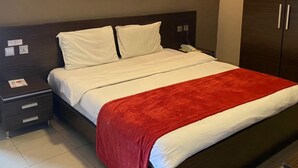 A hotel room with a bed, a nightstand, a wardrobe, and a painting on the wall. - Carliza Hotel Lekki (Lekki)