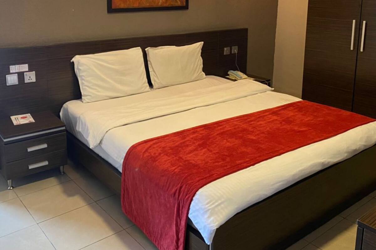 A hotel room with a bed, a nightstand, a wardrobe, and a painting on the wall.