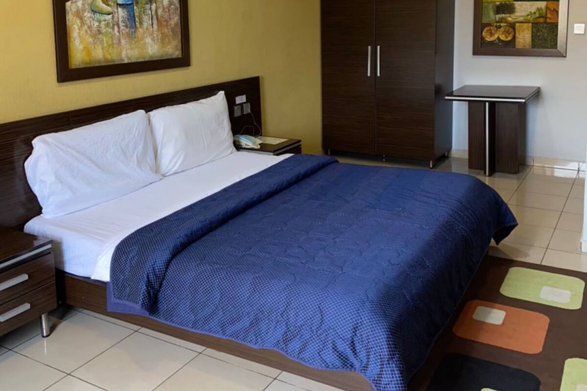 A hotel room with a bed, a wardrobe, a nightstand, and two paintings on the walls.