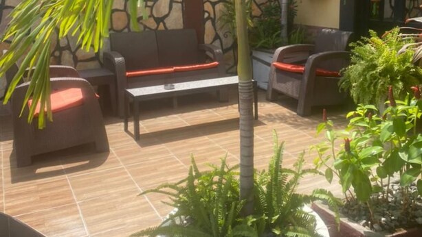 An outdoor seating area with a stone wall, a palm tree, and potted plants. - Carliza Hotel Lekki (Lekki)