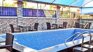 A rectangular outdoor pool with blue mosaic tiles, surrounded by dark brown tiled flooring. - Carliza Hotel Lekki (Lekki)