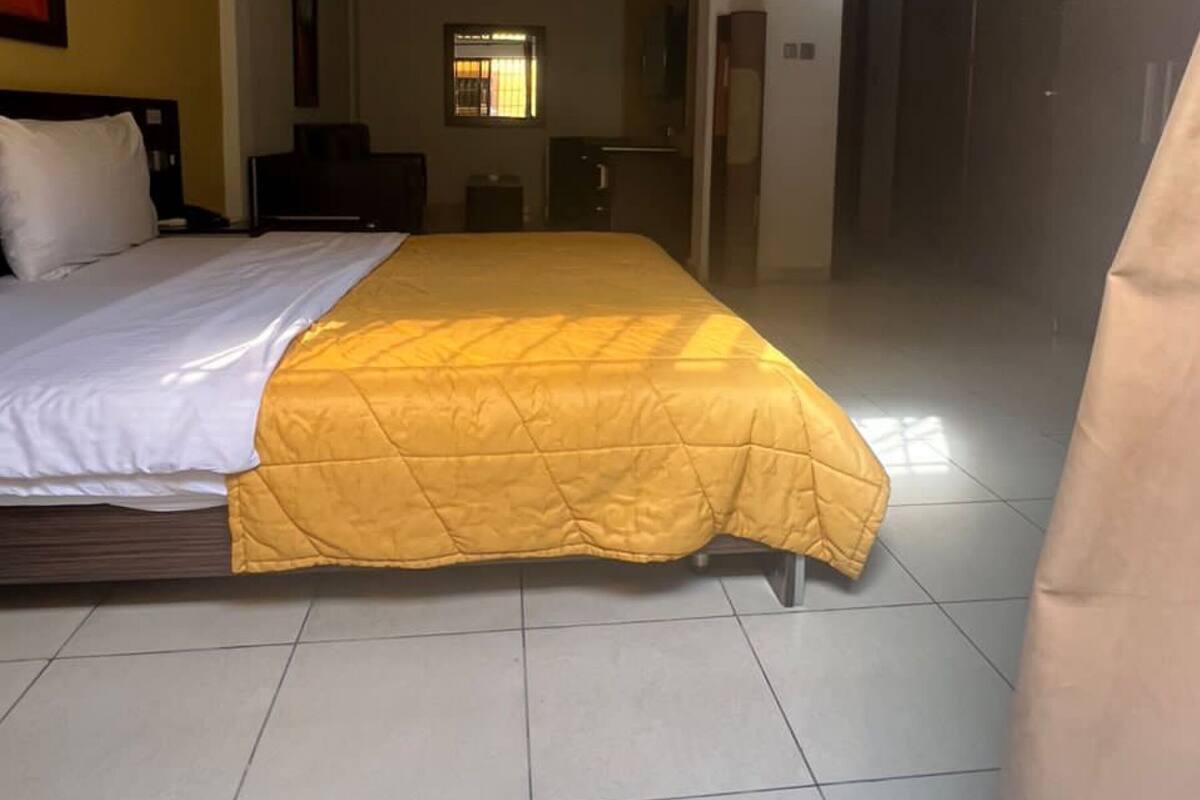 A hotel room with a large bed, a desk, and a chair. There is a window with bars and a door to the right.