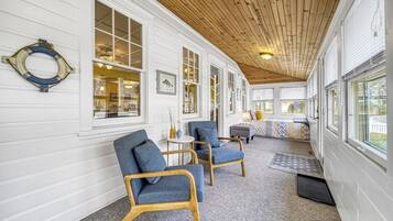 Une véranda couverte avec un plafond en bois et des murs blancs, agrémentée de deux fauteuils bleus et d’une petite table ronde.