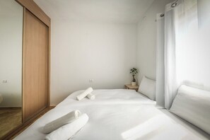 A hotel room with a bed, a wooden wardrobe, a nightstand with a plant, and a window with curtains. - Mamad Luminous 3BR Escape with Balcony by SeaNRent (Tel Aviv)