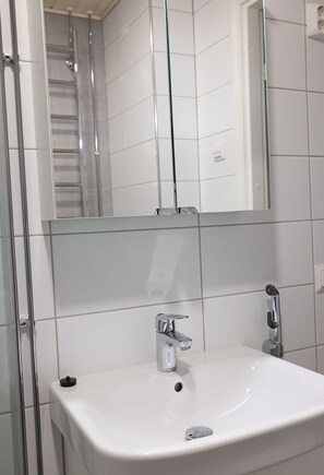 Une salle de bain avec un lavabo blanc, un robinet chromé et une cabine de douche en verre.