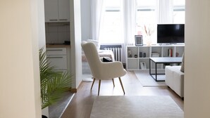 En moderne stue med en hvid sofa, en blød lænestol, et fjernsyn og en bogreol.