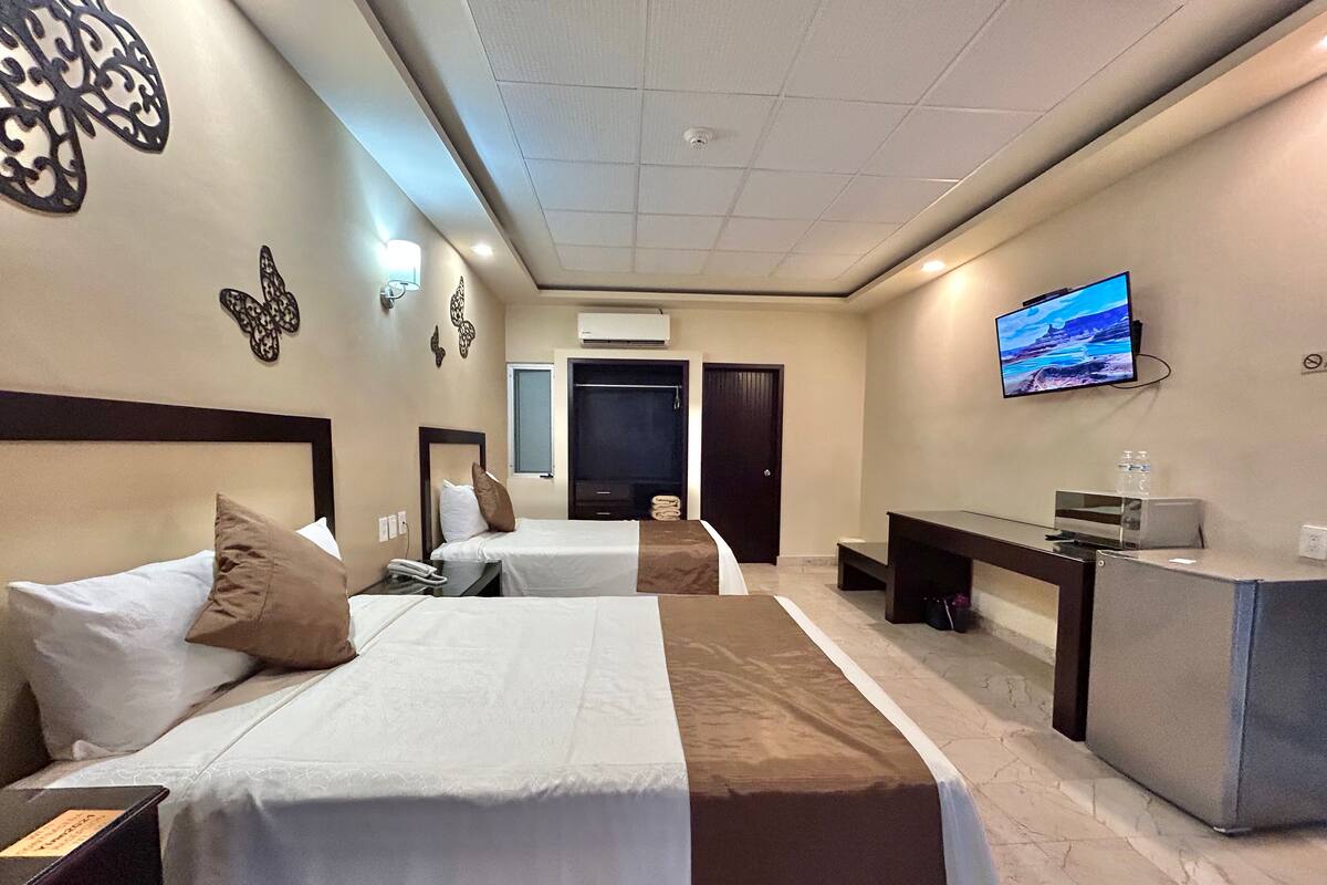 A hotel room with two beds, a desk, a TV, and a bathroom visible through an open door.