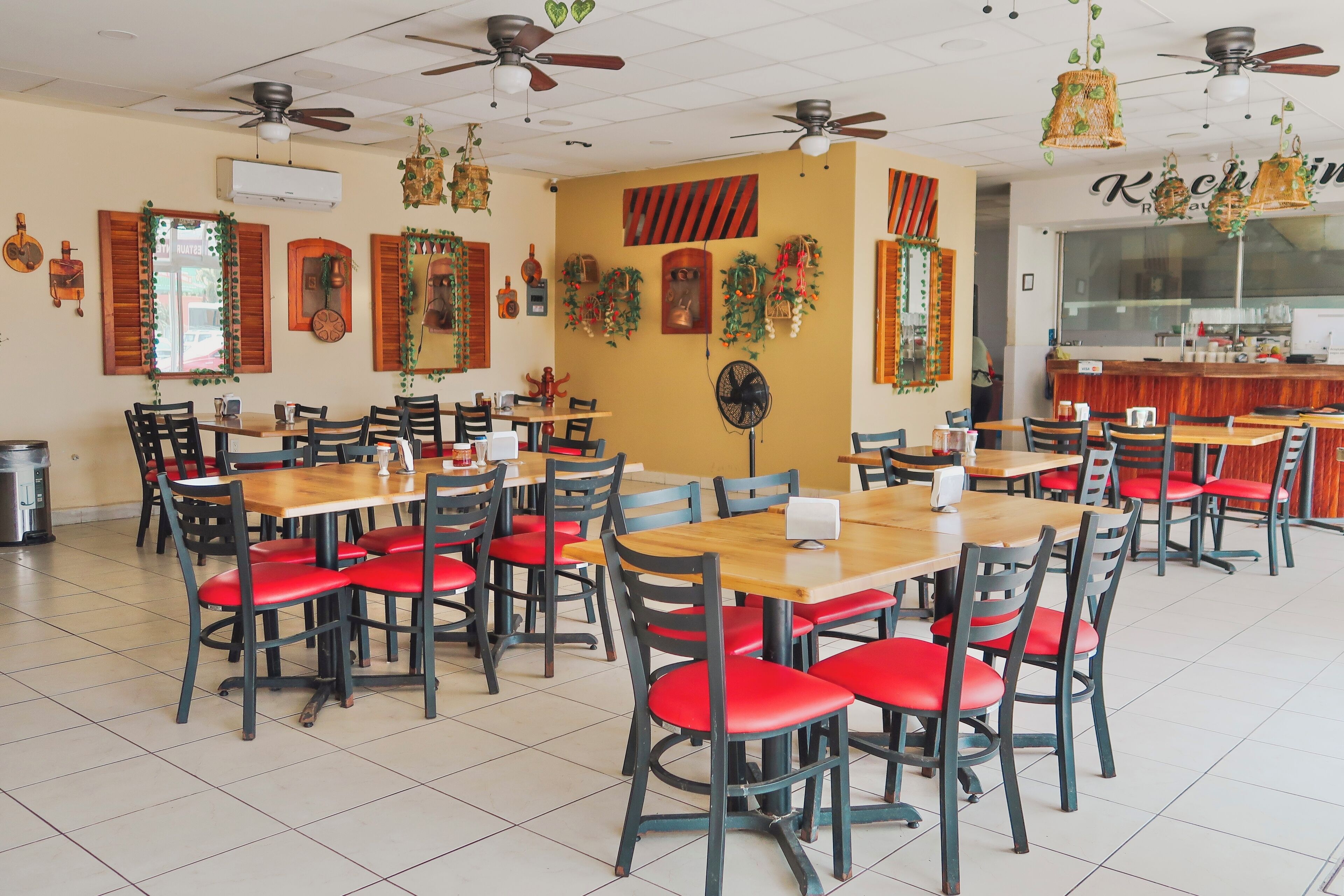 A restaurant with multiple wooden tables and chairs, ceiling fans, and decorative wall hangings.