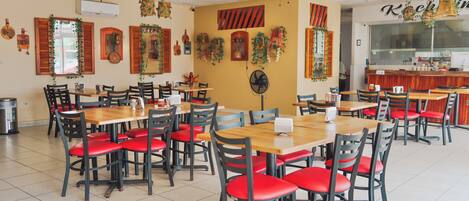A restaurant with multiple wooden tables and chairs, ceiling fans, and decorative wall hangings.