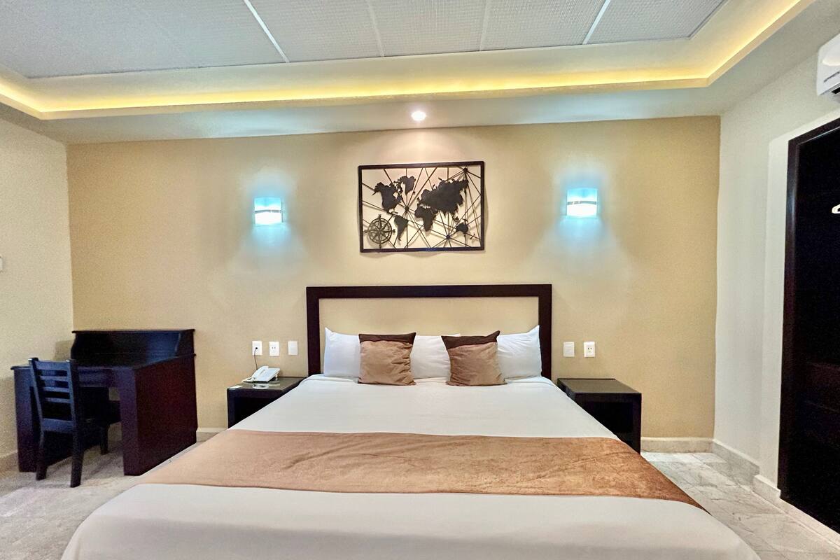 A hotel room with a large bed, a desk, and two wall-mounted lights.