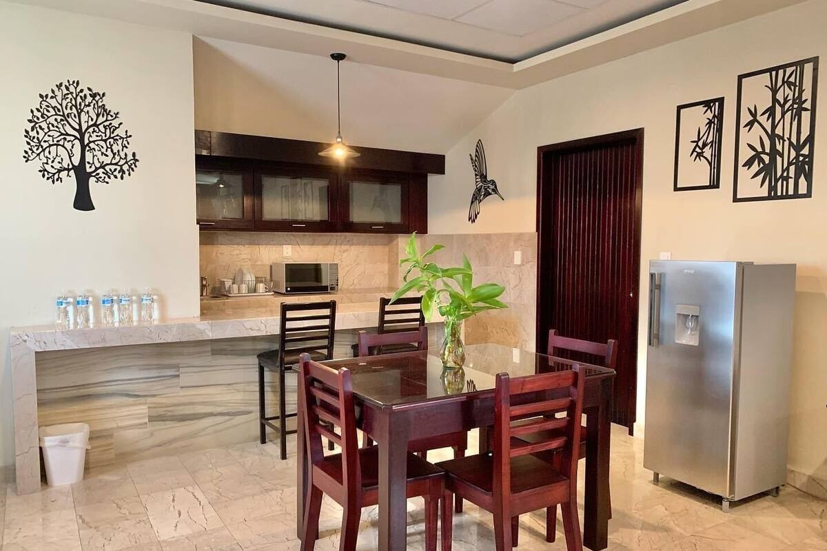 A modern kitchen with a dining area, featuring a marble countertop, a stainless steel refrigerator, and a dining table with chairs.