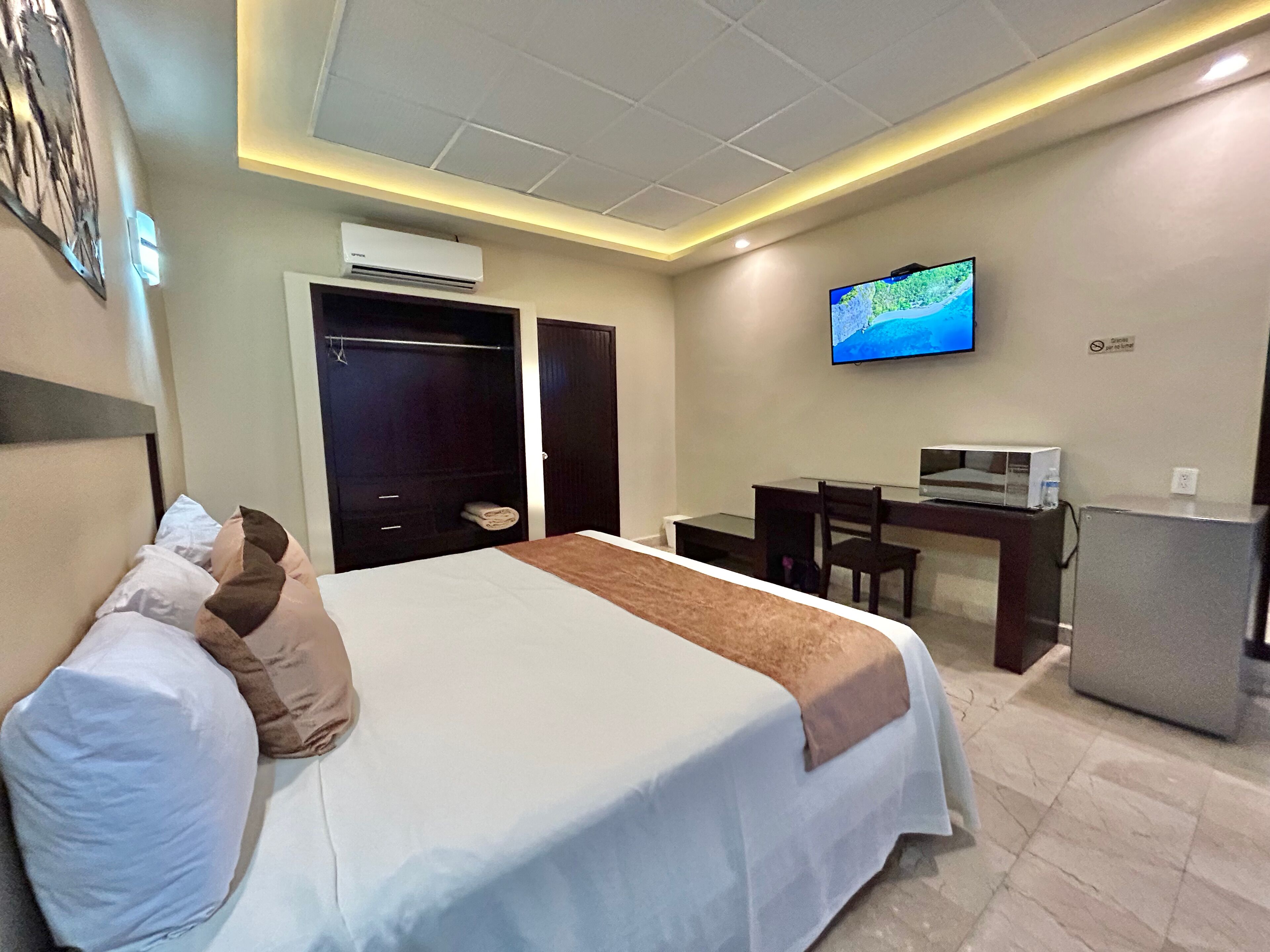 A hotel room with a bed, a desk, a TV, and an air conditioner.