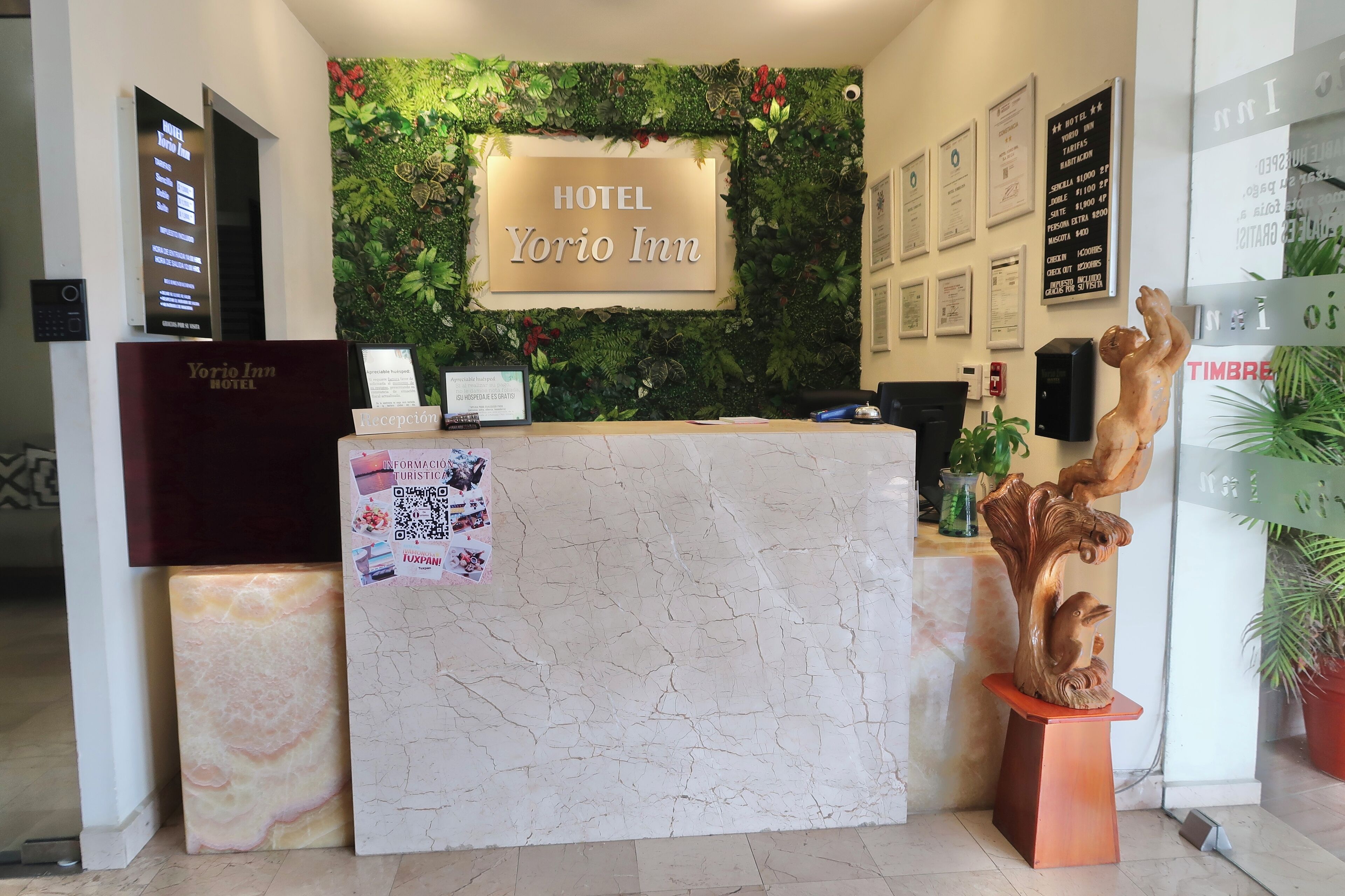 A reception desk at the Yorio Inn hotel with a sign above it, a wall with greenery, and framed certificates on the wall.