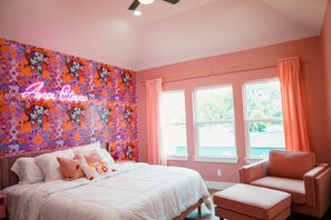 A pink-themed bedroom with a bed, a chair, and a window with curtains.