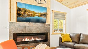 Ein Wohnzimmer mit einem Kamin aus Stein, einem darüber montierten Flachbildfernseher, einem Ledersofa mit gelbem Kissen und einer Holzbalkendecke.
