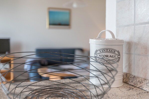 A kitchen counter with a white storage container labeled 'VINTAGE STORAGE' and a metal wire basket.
