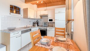 A kitchen with white cabinets, a wooden ceiling, and a dining table set with plates and glasses.