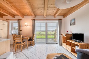 A wooden interior with a dining area, a television, and a sliding glass door to a garden.