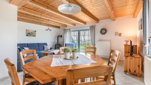 Una mesa de comedor de madera con sillas, un sofá y una chimenea en una habitación con vigas de madera y un ventanal grande.