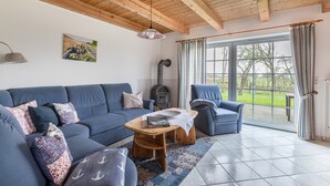 Una sala de estar con sofá, sillones, una mesa de centro de madera, chimenea y un ventanal con cortinas.