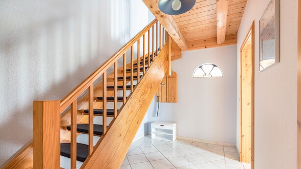 Una escalera de madera con una pared blanca y un ventanal de arco semicircular.