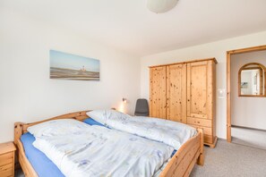 Une chambre à coucher avec un lit en bois, une table de chevet, une chaise, une armoire et un tableau accroché au mur.