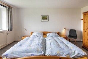 Ein Doppelbett mit floralem Bettzeug, ein Holz-Kopfstück, ein kleiner Nachttisch, ein Stuhl, eine Heizung und ein Holzschrank.