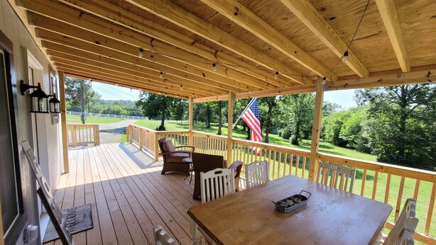 Une terrasse en bois avec une table et des chaises, un drapeau américain et une vue sur un paysage verdoyant.