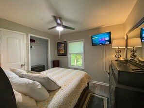Ein Schlafzimmer mit einem Bett, einem Deckenventilator, einem an der Wand montierten Fernseher und einer Kommode mit Lampen.