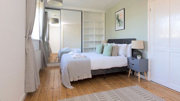 A bedroom with a bed, bedside table, and a wardrobe. - Cosy Room in Morden (Morden)