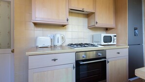 A compact kitchen with wooden cabinets, a microwave, a toaster, and a gas stove. - Cosy Room in Morden (Morden)