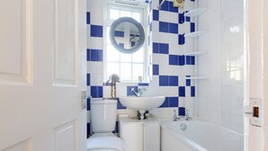 A bathroom with a toilet, sink, and bathtub, featuring blue and white tiles. - Cosy Room in Morden (Morden)