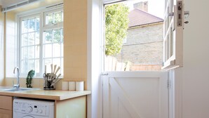 A kitchen with a washing machine, a sink, and a window with a view of a brick building and a tree. - Cosy Room in Morden (Morden)