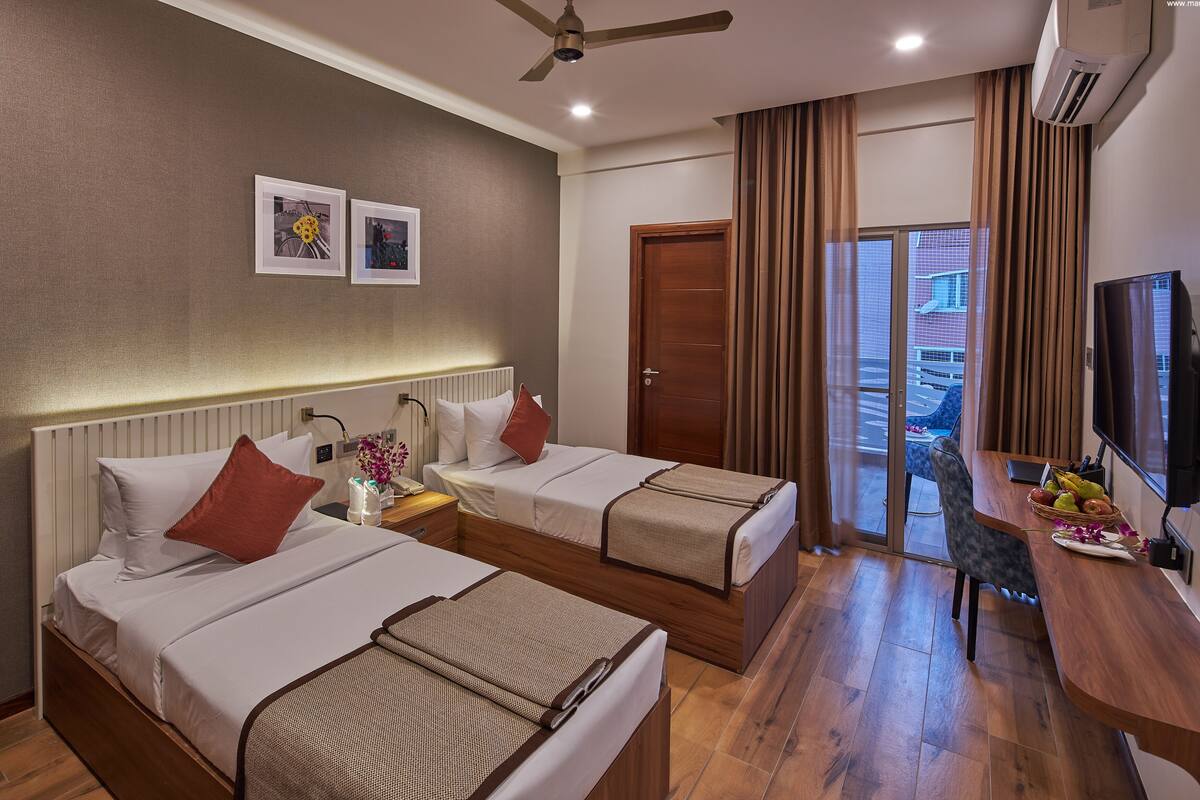 A hotel room with two beds, a desk with a TV, and a view of the outside.