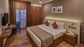 Quarto de hotel com cama, mesa de cabeceira, escrivaninha, cadeira e ventilador de teto.