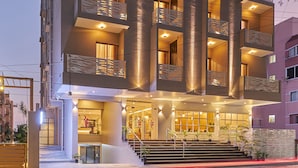 Um hotel com vários andares, varandas, uma entrada bem iluminada e uma escadaria que leva à área principal.