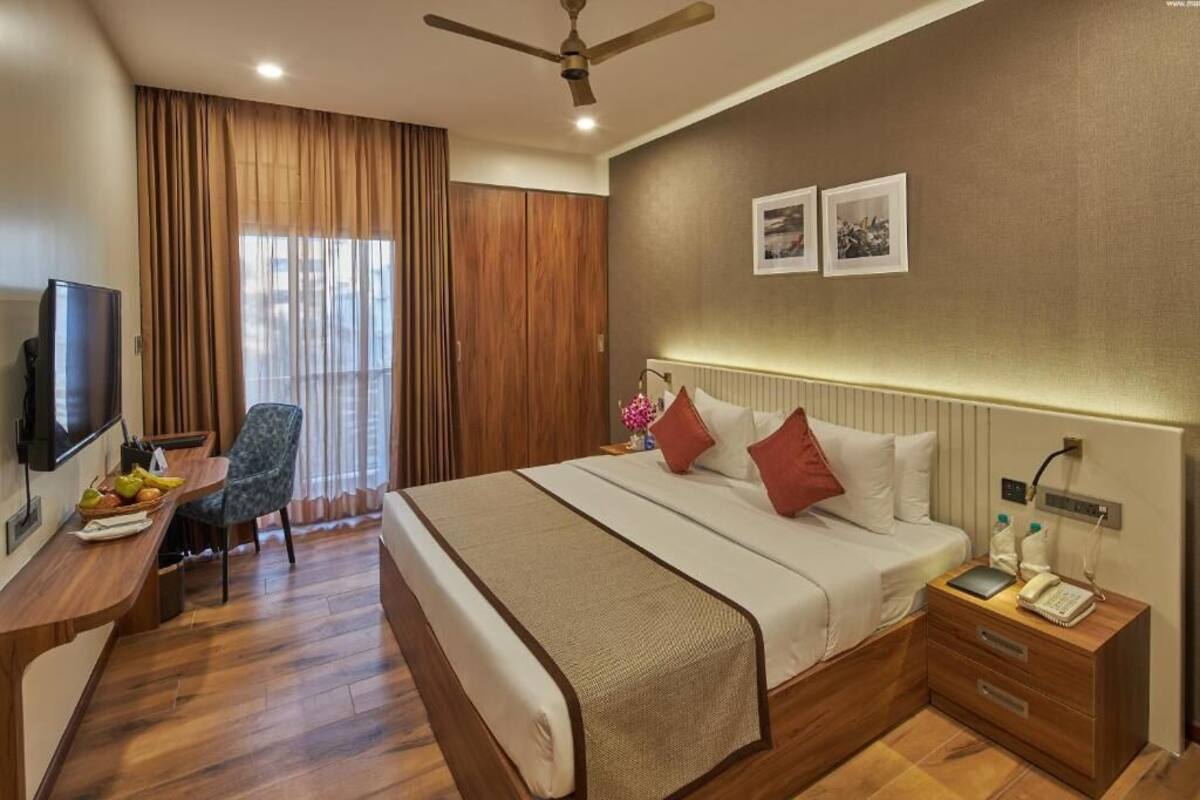 A hotel room with a bed, bedside table, TV, desk, chair, and curtains.