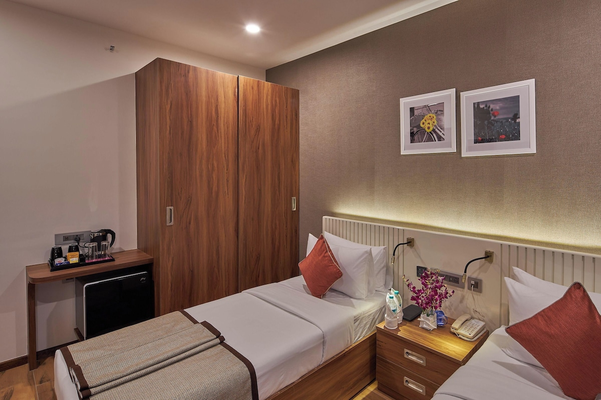 A hotel room with a bed, bedside table, wardrobe, and a small desk with a coffee machine.