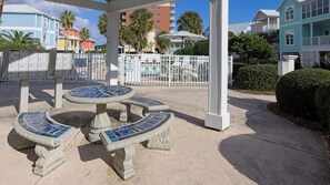 A covered outdoor seating area with mosaic-tiled tables and chairs, surrounded by a white fence, in a resort setting.
