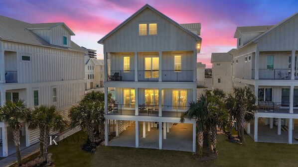 A multi-story beachfront property with balconies, outdoor seating, and a pool area.