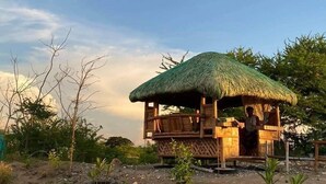 A wooden structure with a thatched roof, surrounded by trees and vegetation. - Family House to enjoy by the beach (Pasuquin)