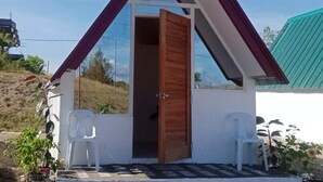 A small, triangular-shaped building with a wooden door and white walls. There are two white plastic chairs outside. - Family House to enjoy by the beach (Pasuquin)
