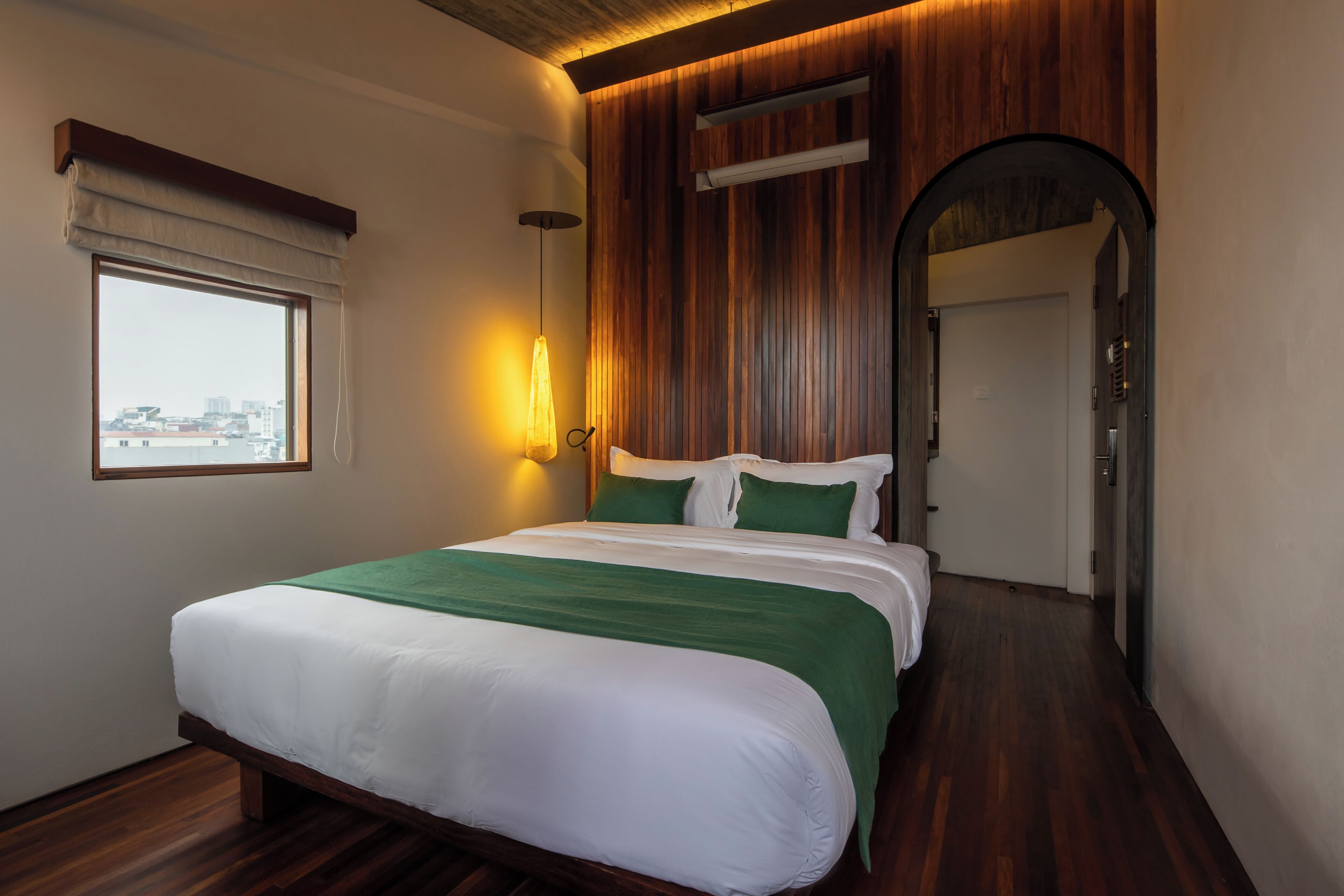 A hotel room with a large bed, a window, a wooden wall, and a door.