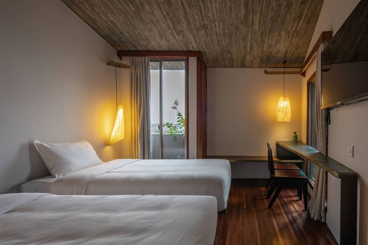 A room with two beds, a desk, and a window with curtains.