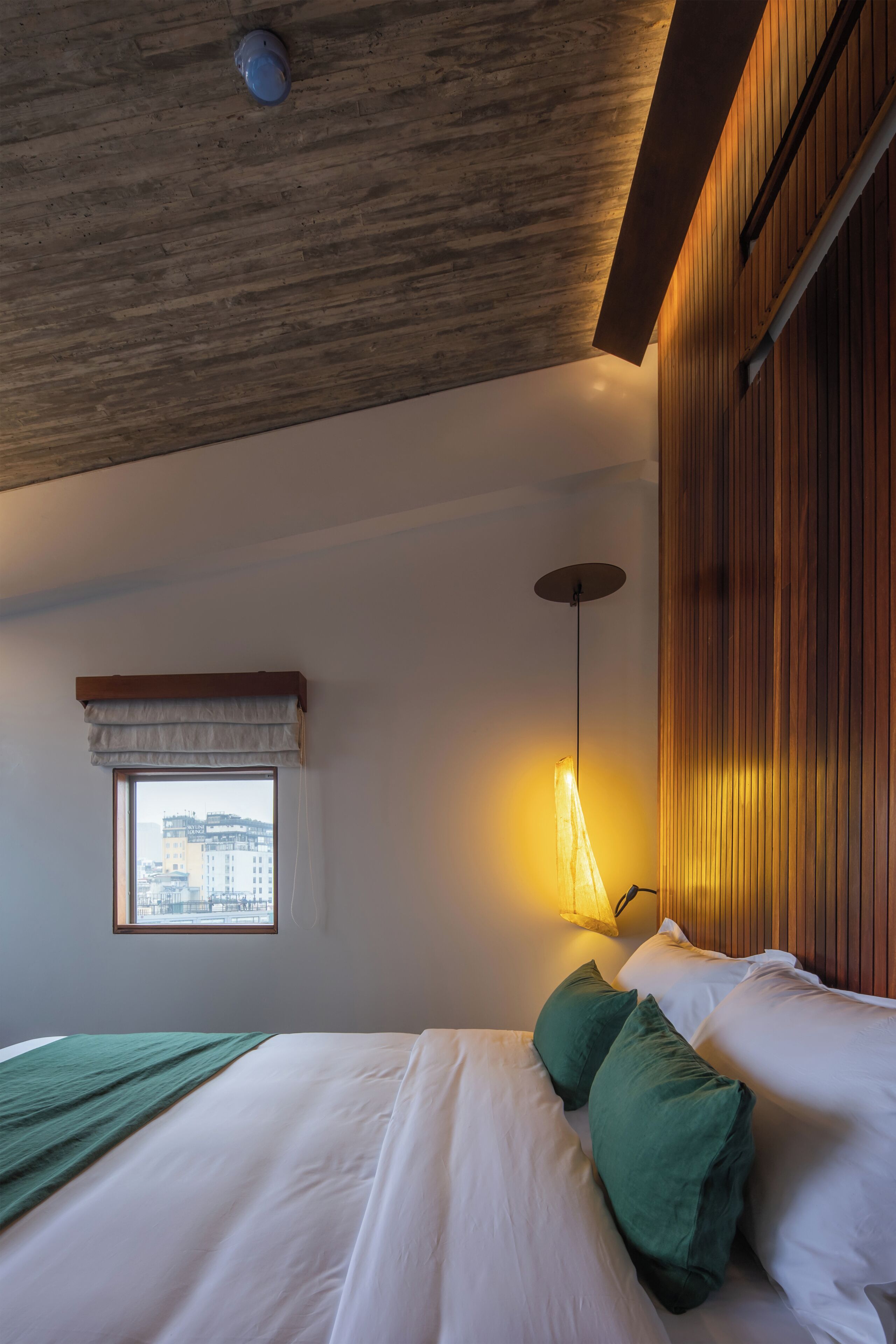 A bedroom with a bed, pillows, a window, and a wall-mounted lamp.