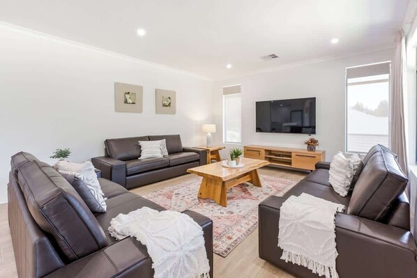 A modern living room with a sofa set, a coffee table, a flat-screen TV, and artwork on the walls.